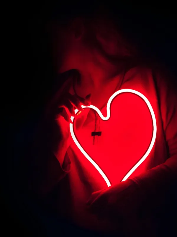 Eine Frau hält ein rotes Neon-Herz in den Händen – ein Sinnbild für Leidenschaft, Intimität und die stilvolle Ästhetik moderner Erotikclubs.