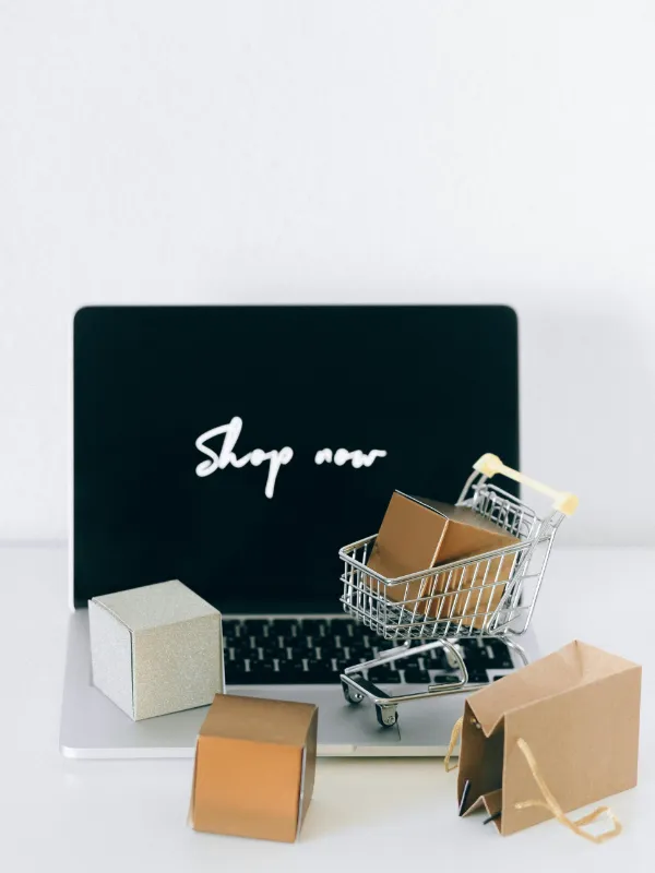 Online-Shopping-Szene mit Laptop, Einkaufstaschen und Miniaturwagen