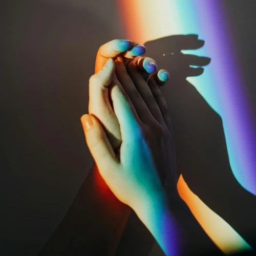Zwei Hände berühren sich im Regenbogenlicht als Zeichen von Nähe und Vielfalt