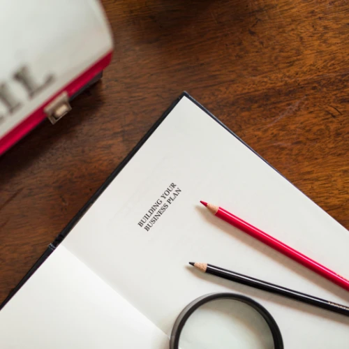 Notizbuch mit Aufschrift „Building your Business Plan“ und Stifte auf einem Tisch
