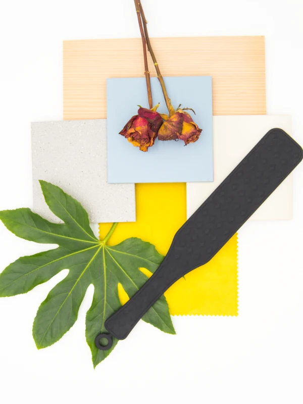 Materialboard mit Holzmuster, Farbflächen und einem schwarzen Paddle für ein BDSM Spielzimmer