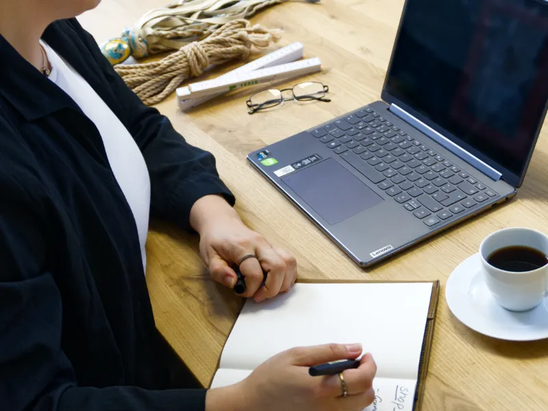 Grietje von Grietje Concept Design schreibt eine Marketing Strategie in ein Notizbuch, daneben Laptop, Kaffee und Bondage-Seil