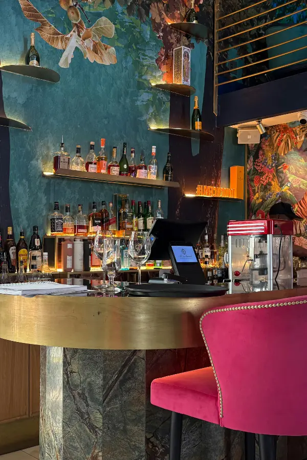 Bar eines modern gestalteten Swingerclubs mit goldener Theke, pinken Samtsesseln und floraler Wandgestaltung