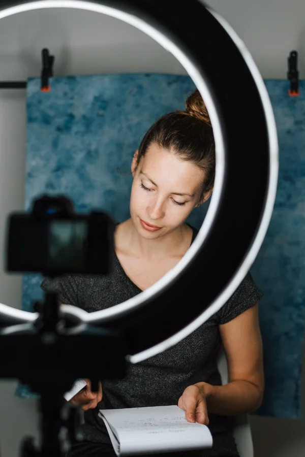 Frau liest Notizen vor einer Kamera mit Ringlicht und bereitet ein Video für Social Media vor